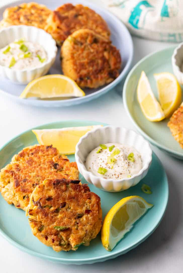 Old fashioned salmon patties recipe on a green plate, with a white ramekin of tartar sauce and two lemon wedges.