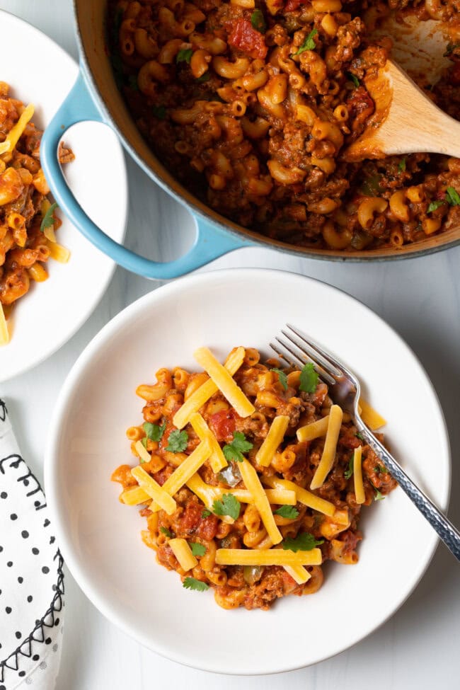 Macaroni and beef bake with shredded cheese on top in a white bowl. 