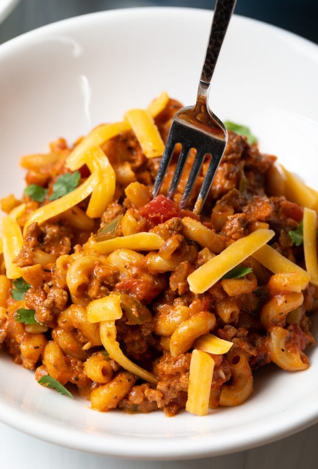 American Goulash served in a bowl with a fork taking a bite. 