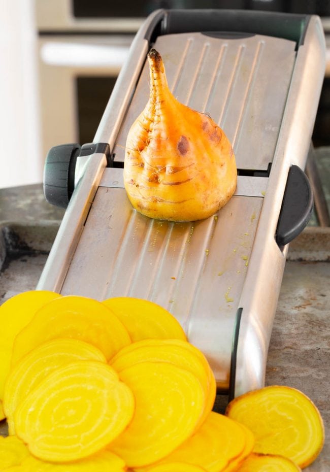 Beets being sliced on a mandoline slicer. 
