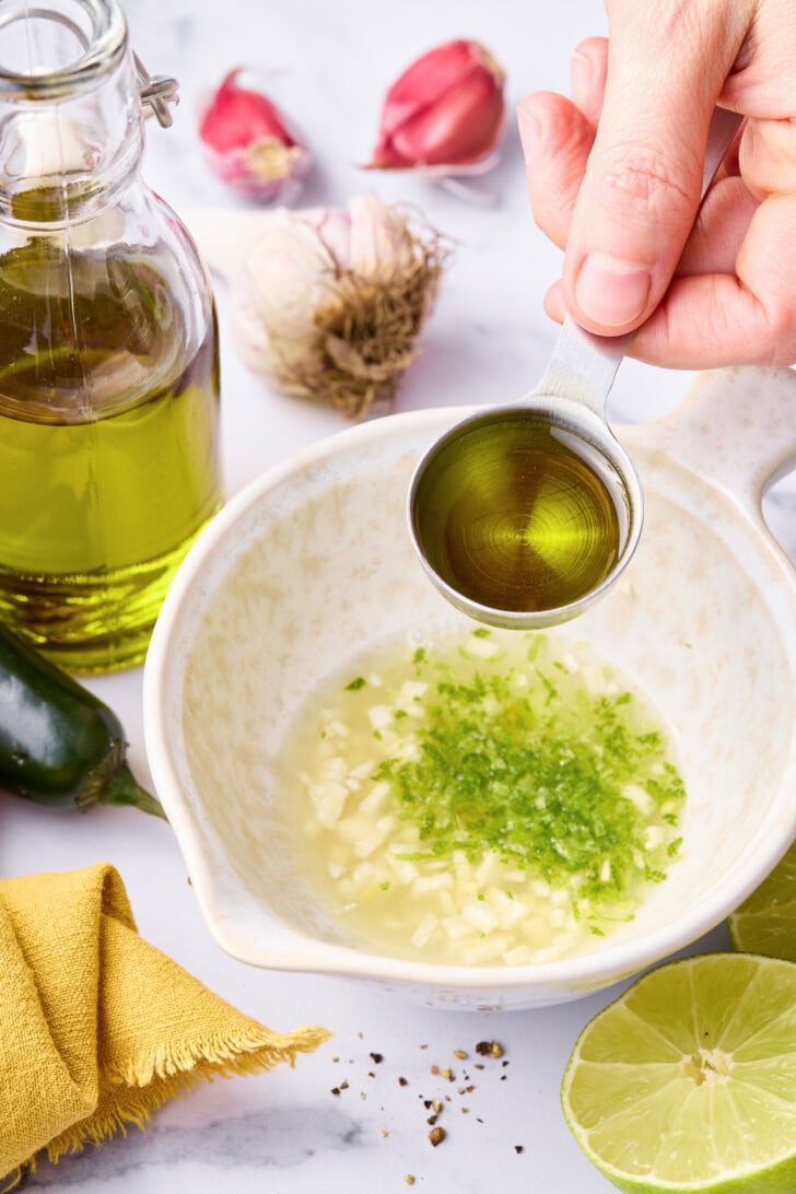 Mixing salmon marinade with olive oil being added to a small bowl. 