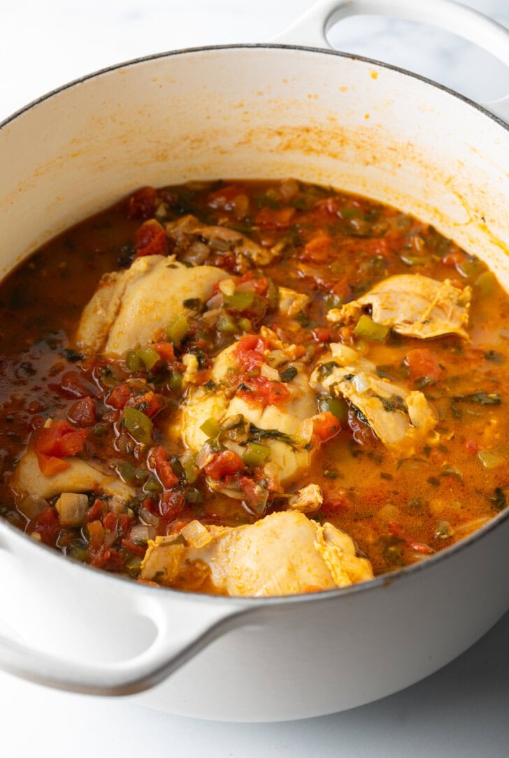 Chicken thighs and veggies in a broth in a large cooking pot.