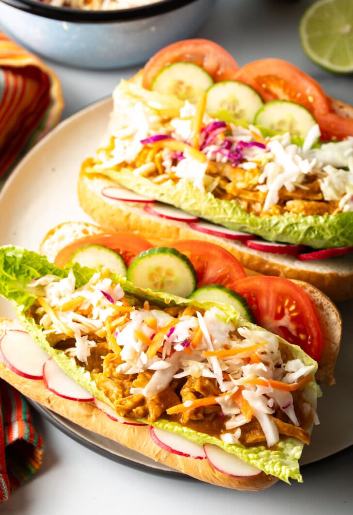 Two open sandwiches each loaded with stewed chicken and veggies, side by side on a large plate.