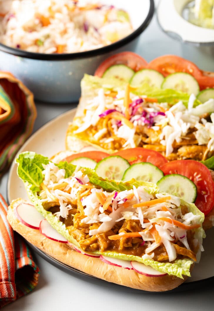 Two open sandwiches each loaded with stewed chicken and veggies, side by side on a large plate.