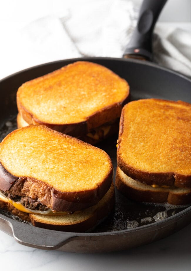 Three sandwiches being toasted in a large skillet.