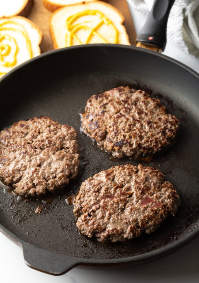 Three cooked ground beef patties in a skillet.