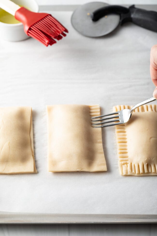 Hand with fork crimping the edges of the unbaked peach pies shut.