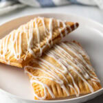 Two homemade peach pop tarts resting against each other on a white plate.