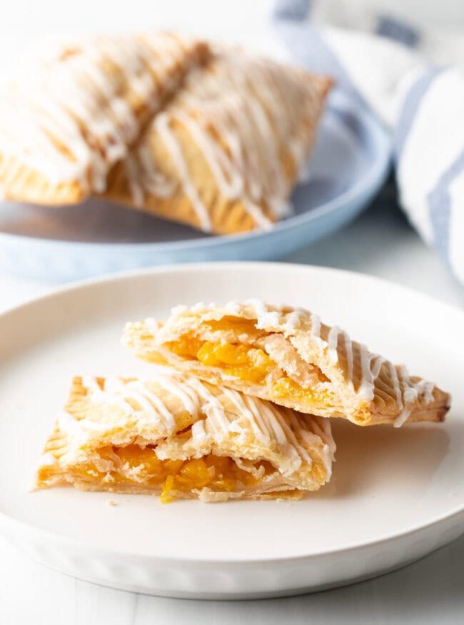 A peach pop tart on a white plate, cut in half to expose the peach filling, with one piece resting on the other.