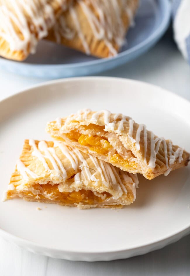 A peach pop tart on a white plate, cut in half to expose the peach filling, with one piece resting on the other.