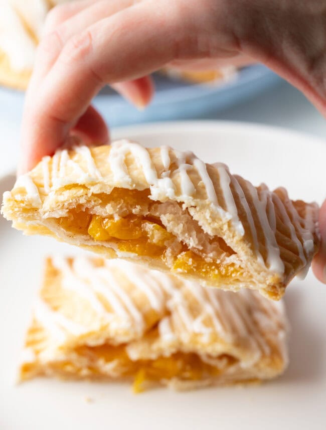 Hand holding half of a hand pie to camera, showing the inside peach mixture.