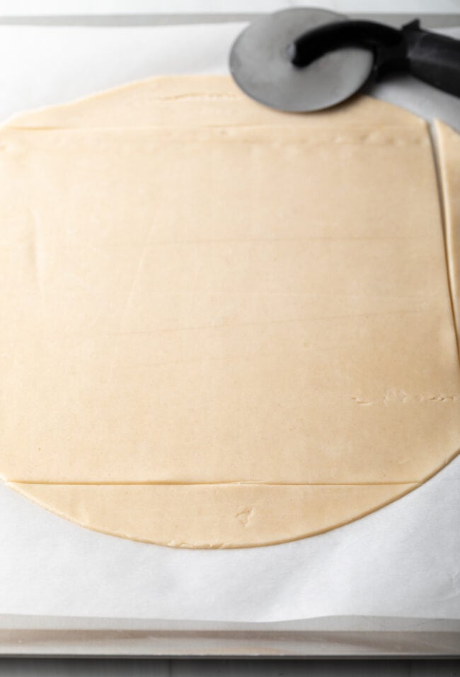 Cutting a circle of premade pie dough into a large square.