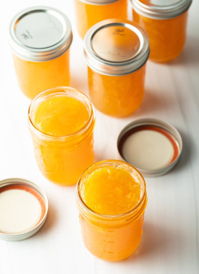 Multiple jars of peach preserves without lids.