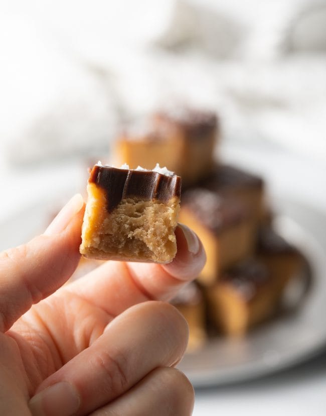 holding handing piece of old fashioned peanut butter candy with chocolate top and bite taken out