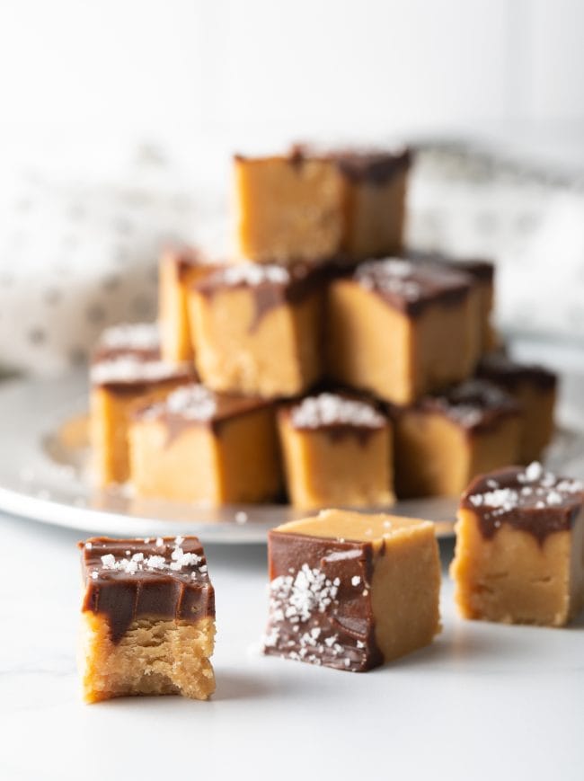 background with stacked candy, three pieces of fudge in foreground one piece with bite taken 