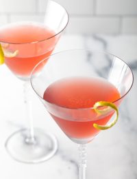 Top down view of two cosmopolitan cocktails in a cocktail glass with twist of lemon.