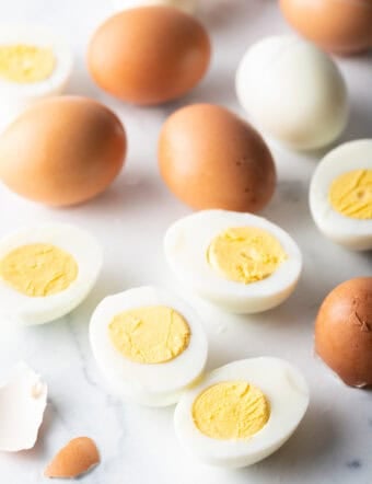 A dozen hard boiled eggs on a white marble backdrop. There are five egg halves, four brown eggs in the shell, and one white peeled egg.