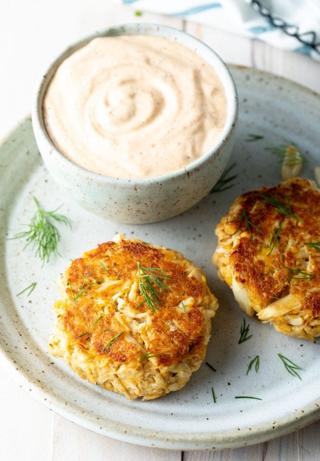 Two maryland crab cakes on a plate with a side of tar tar sauce. 