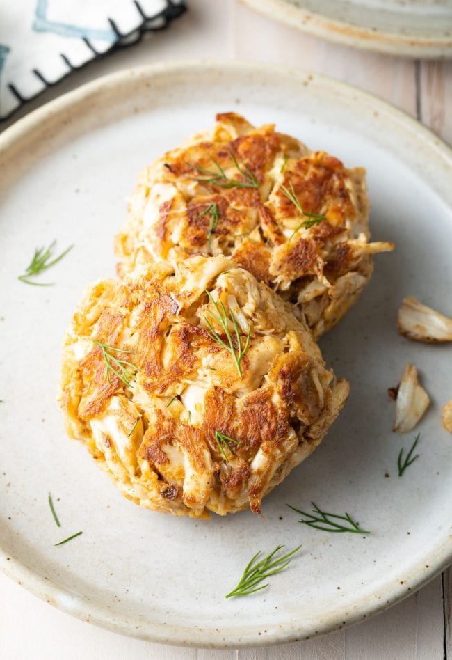 Crab cakes stacked on top of each other on a white plate. 