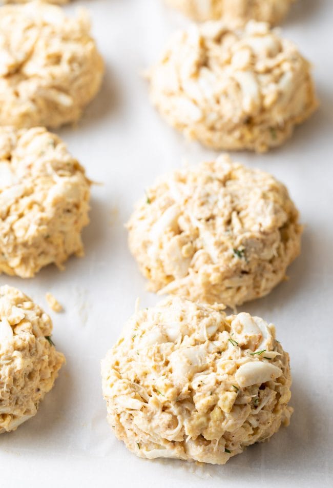 Crab cakes lined up on a baking sheet lined with parchment before being baked. 