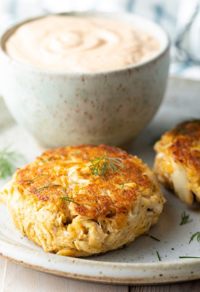 Crab cakes on a plate with a sprinkle of dill on top. 