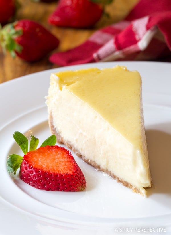 A slice of Slow Cooker Cheesecake on a white plate with a strawberry garnish.