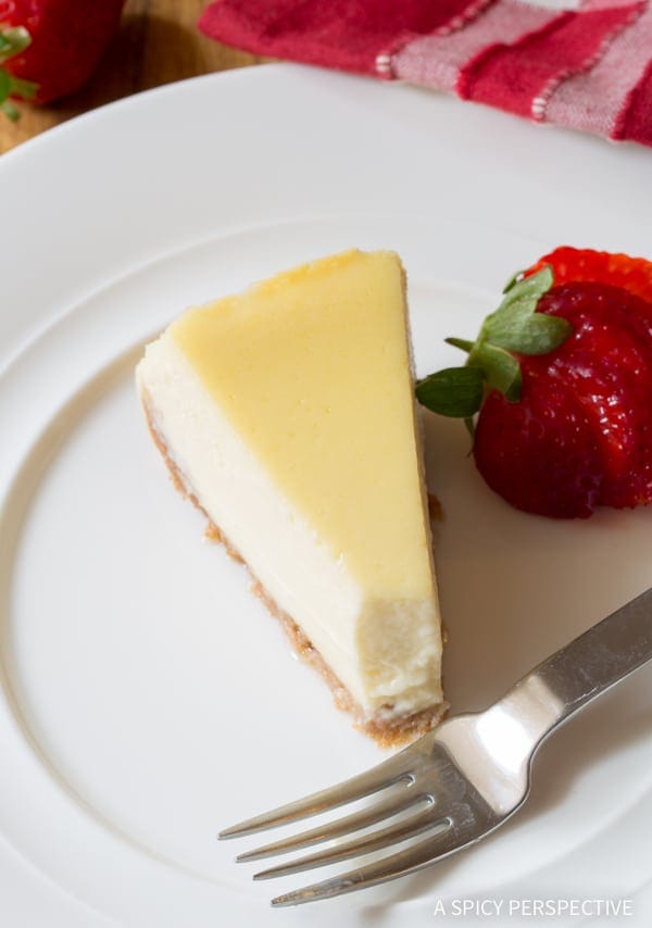 A top down shot of slow cooker cheesecake with a bite taken out of it. A fork and strawberry are next to the slice.