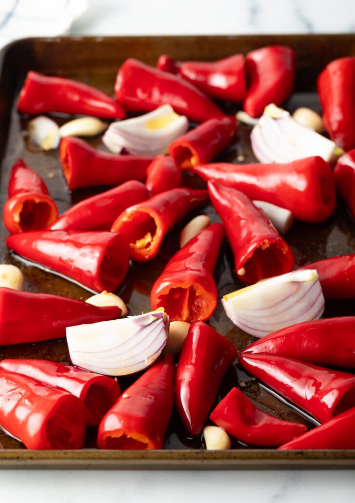 Raw red chili peppers and onions on a baking sheet.