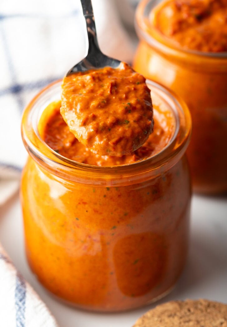 Two glass jars of thick peri peri sauce. A metal spoon is in the jar closest to camera.