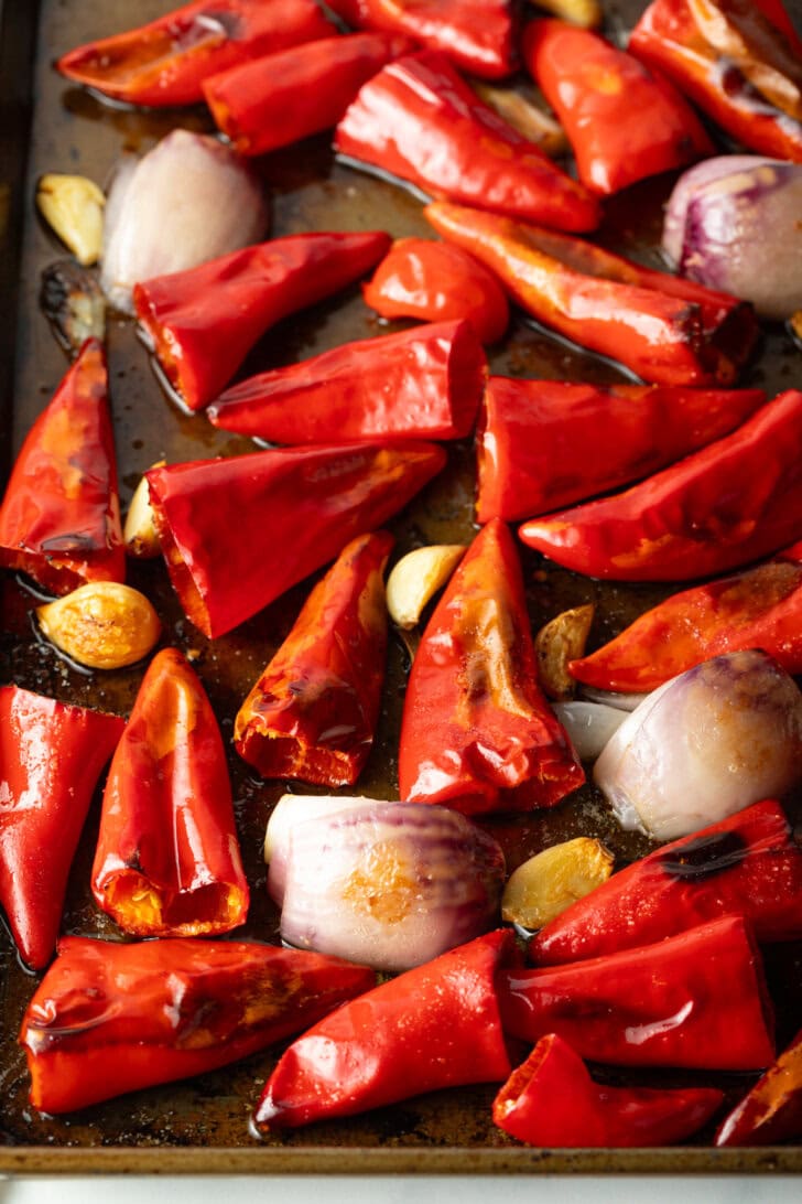 Roasted red chili peppers and onions on a baking sheet.