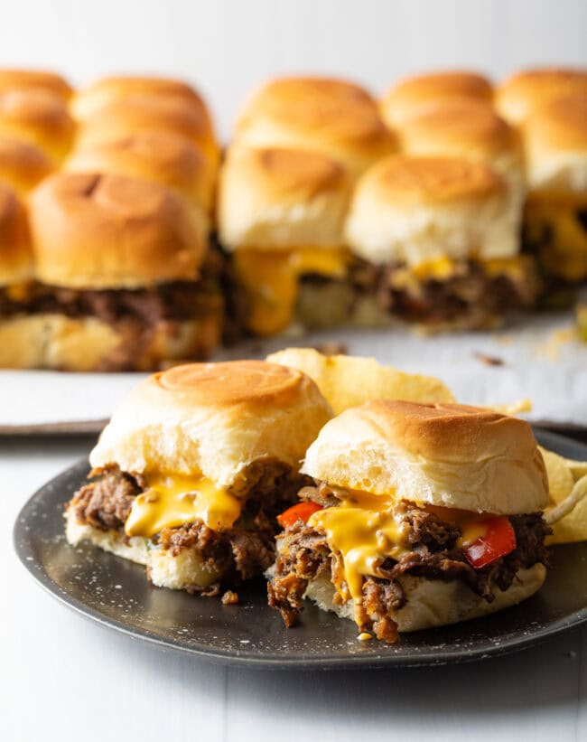 Sliders in background, two philly cheesesteak sandwiches on a plate.