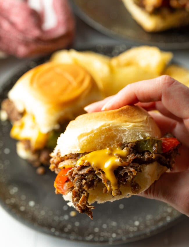 Hand holding a mini philly cheese steak sandwich to camera.