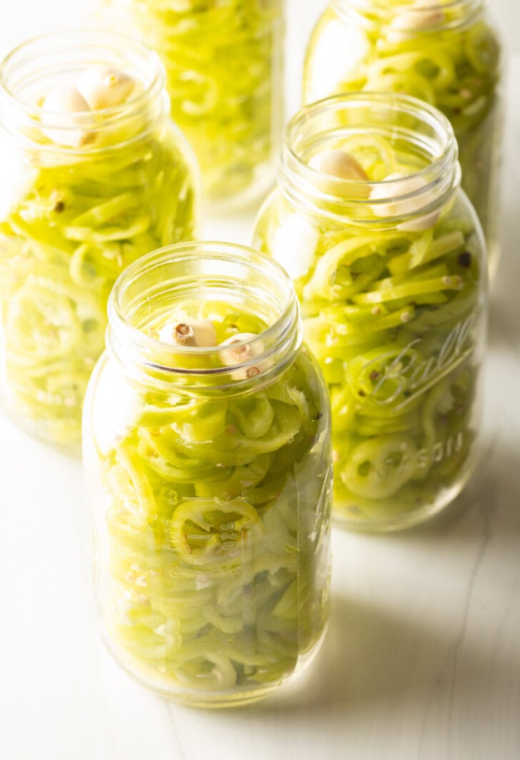 Full jars of pickled peppers. The lids are off to show the slices of peppers.