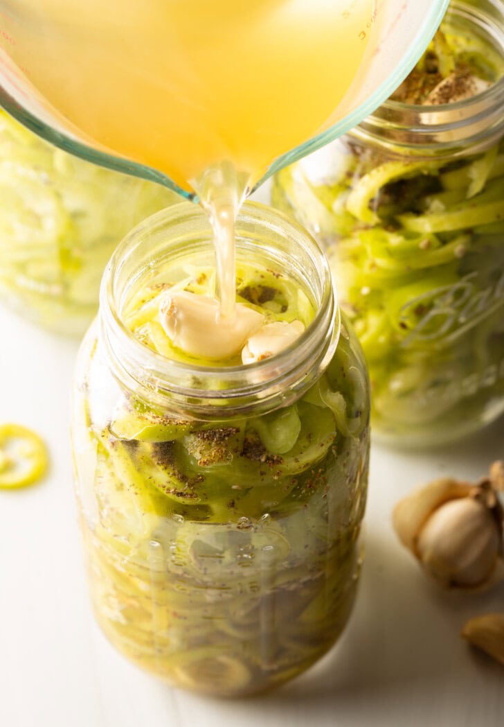 Pouring pickling brine into a jar of sliced peppers.