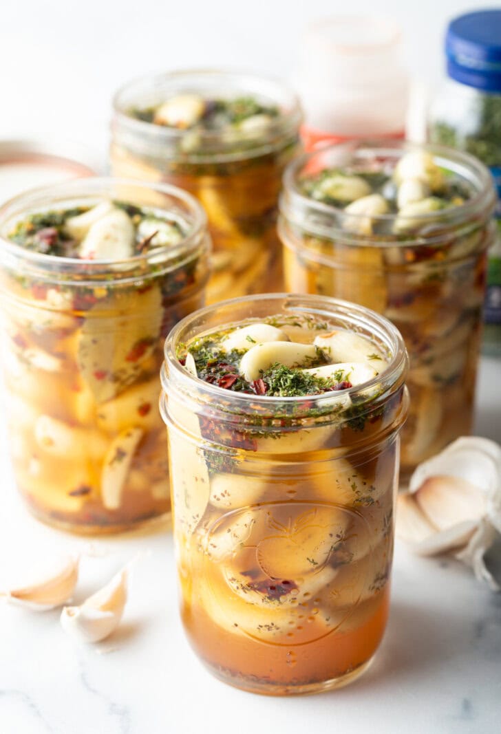 Several open glass jars stuffed with preserved garlic and herbs.