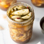 Top down open glass jar stuffed with preserved garlic and herbs.