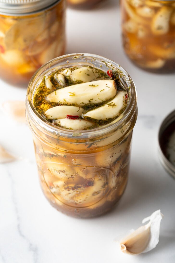 Top down open glass jar stuffed with preserved garlic and herbs.