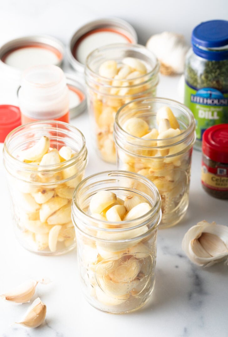 Four glass mason jars stuffed with fresh raw garlic cloves.