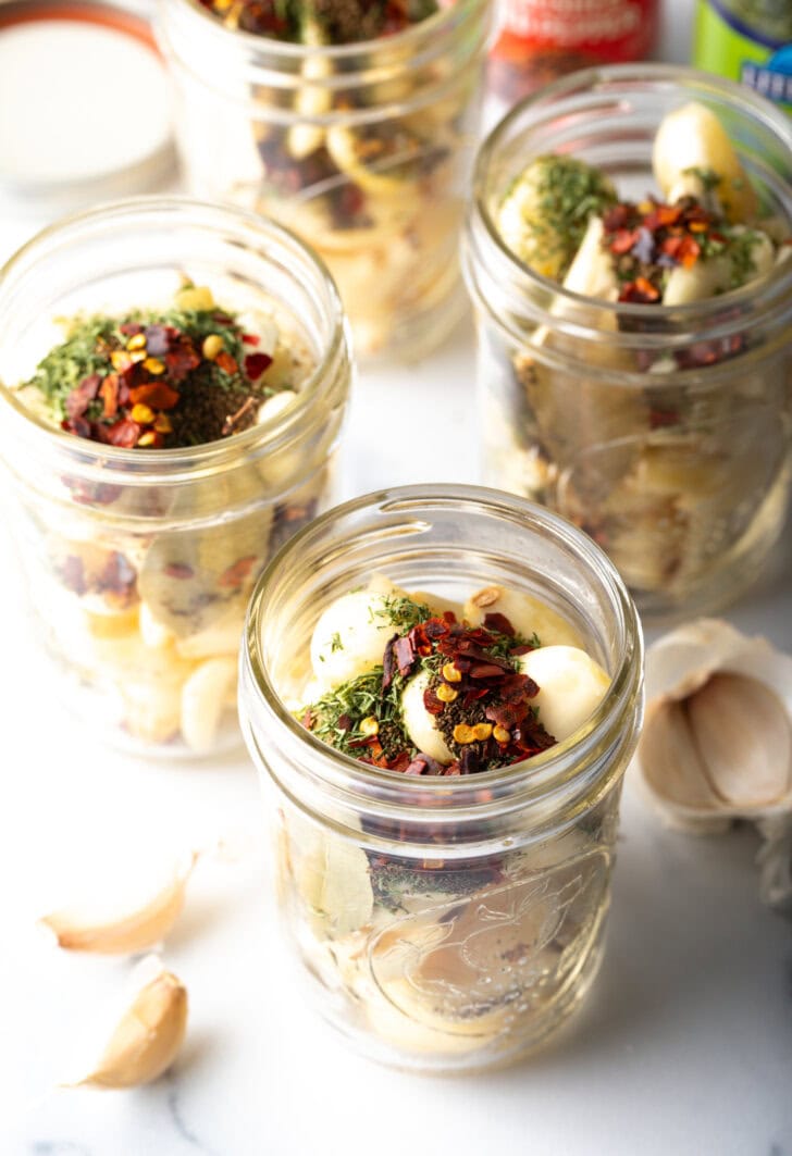 Top down open glass jar stuffed with preserved garlic and herbs.