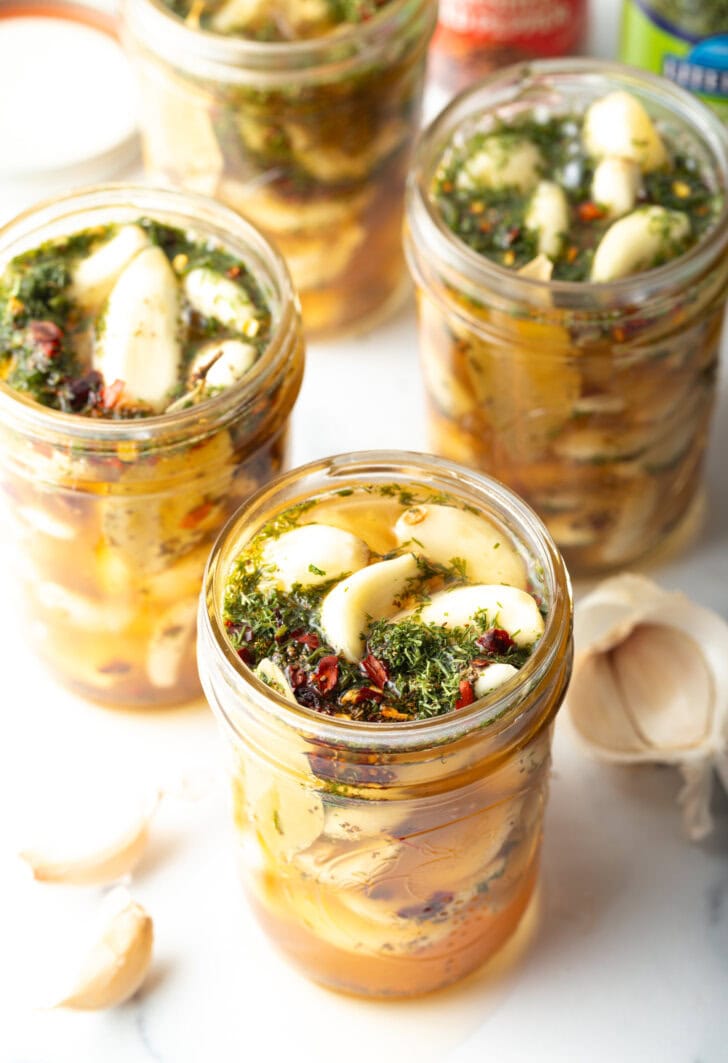 Top down open glass jar stuffed with preserved garlic and herbs.