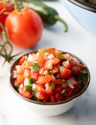 A white bowl of fresh pico de gallo with chopped tomatoes, onion, jalapeno, and cilantro.