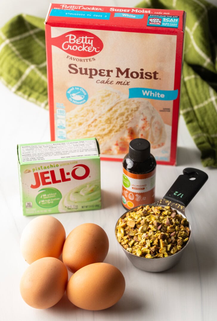 Recipe ingredients: 4 whole eggs, measuring scoop with chopped pistachios, box of pistachio pudding mix, box of white cake mix, and bottle of vanilla.