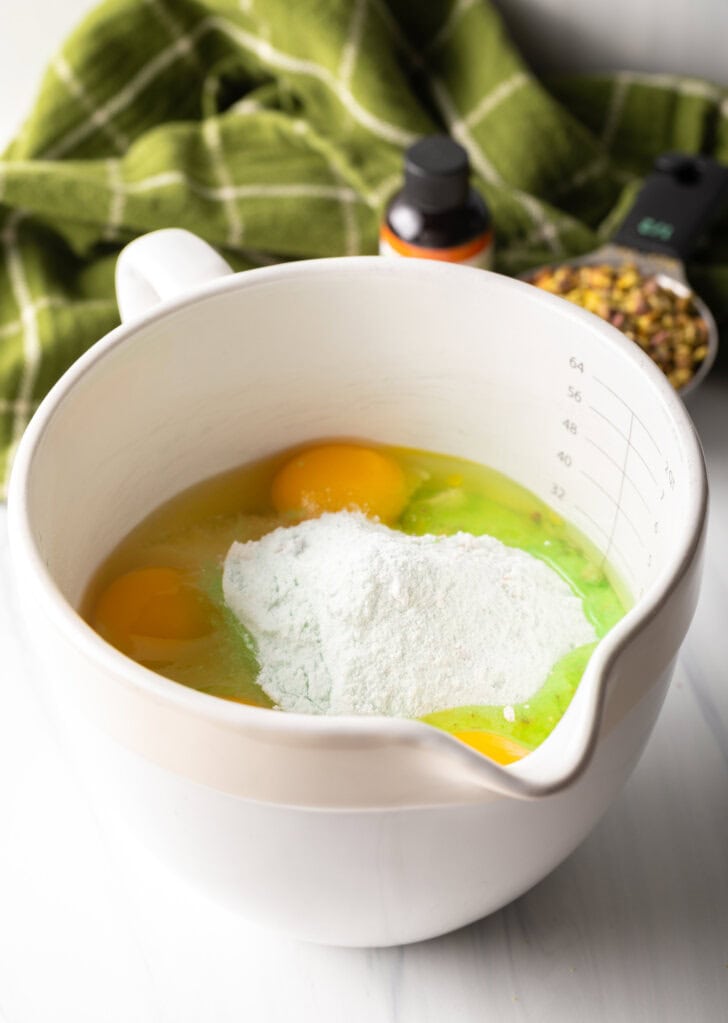 White mixing bowl with powdered pudding mix, eggs, flour, and all cake ingredients