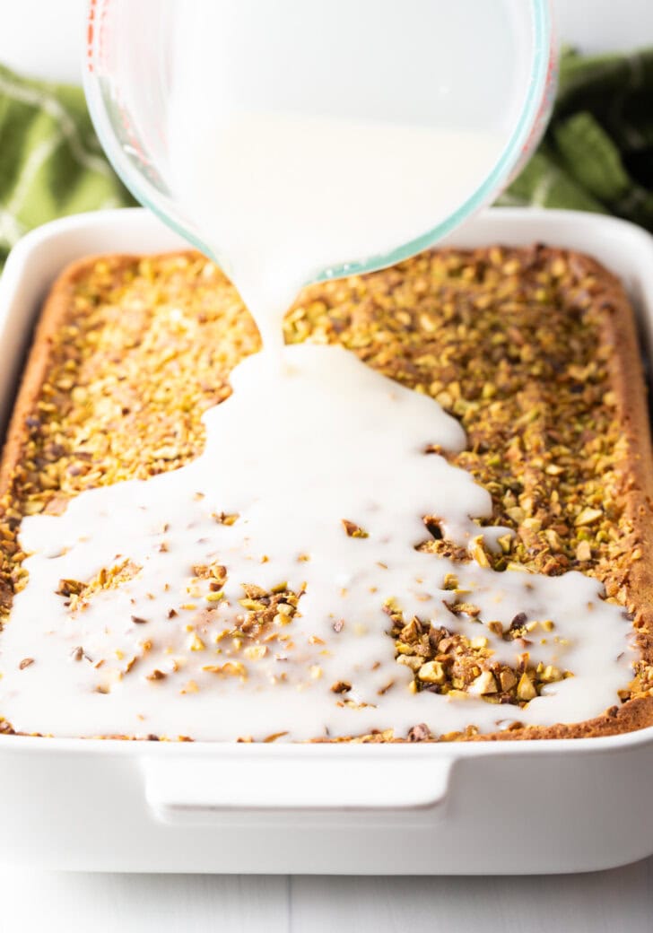 Glass mixing bowl pouring white glaze over the top of the baked cake.