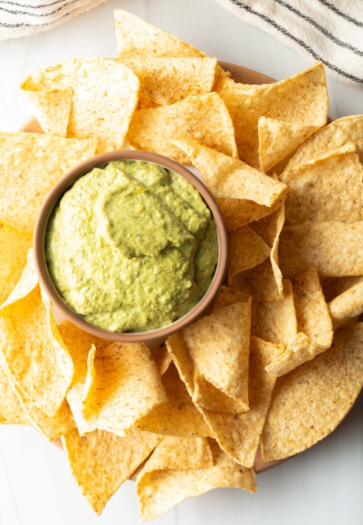 Top down small bowl of poblano cream sauce surrounded by tortilla chips