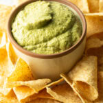 Small bowl of poblano cream sauce surrounded by tortilla chips