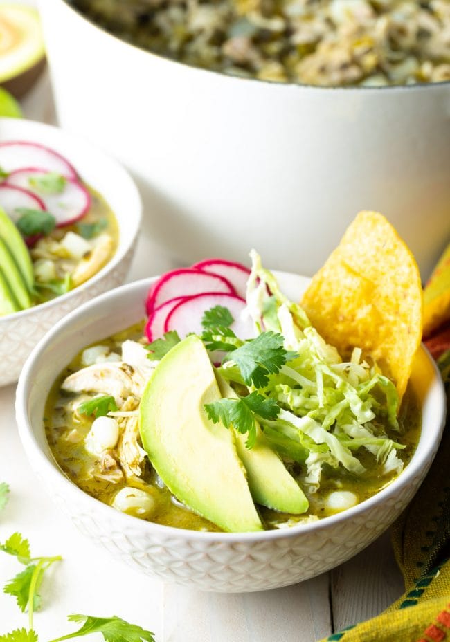 Posole verde chicken stew in a bowl with avocado, cabbage and radishes on top. 