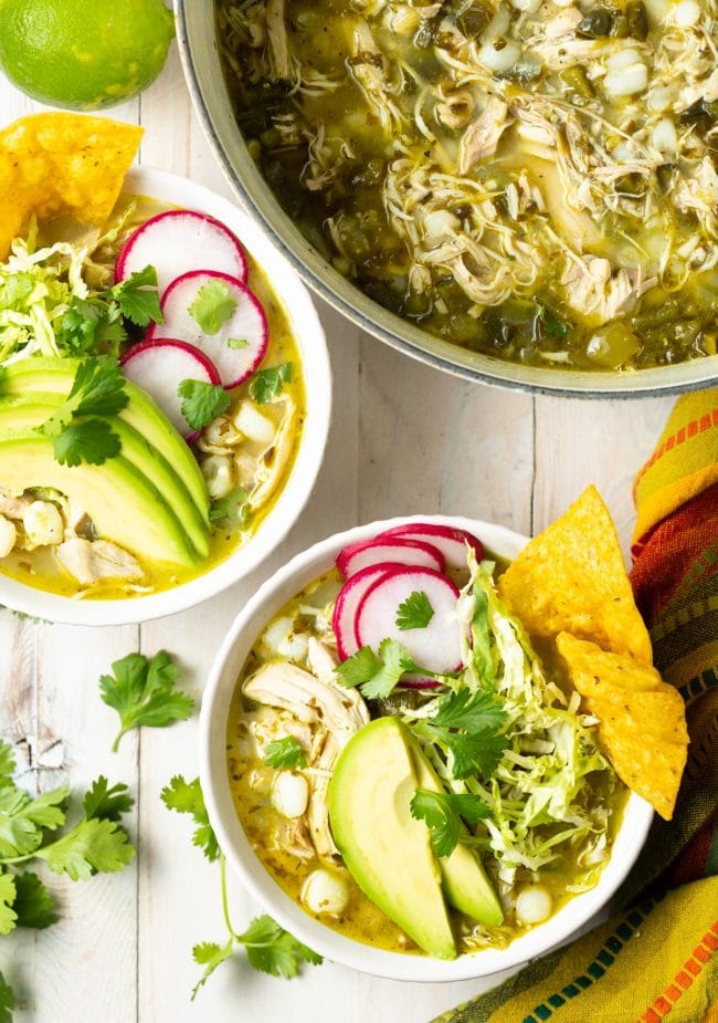 Pozole Verde de Pollo - Chicken posole served in white bowls topped with cabbage, radish, avocado and tortilla chips. 