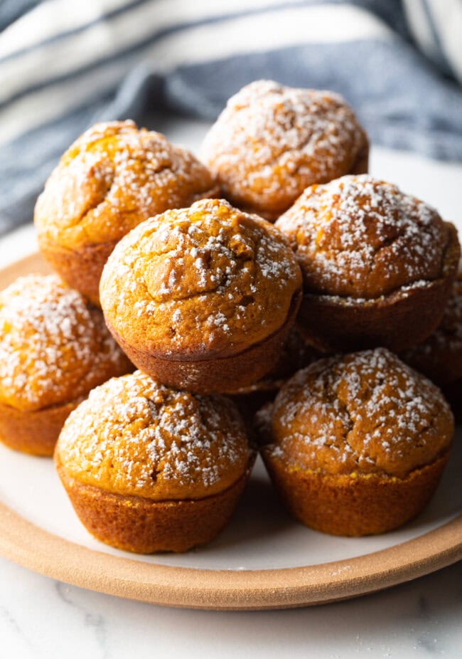 Stack of fluffy muffins made with pumpkin puree, each dusted with powdered sugar.