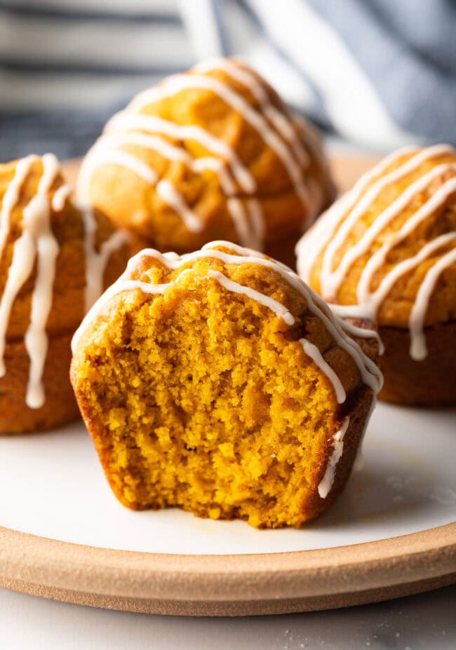 Plate with four pumpkin muffins drizzled with glaze. One muffin has bite taken out.